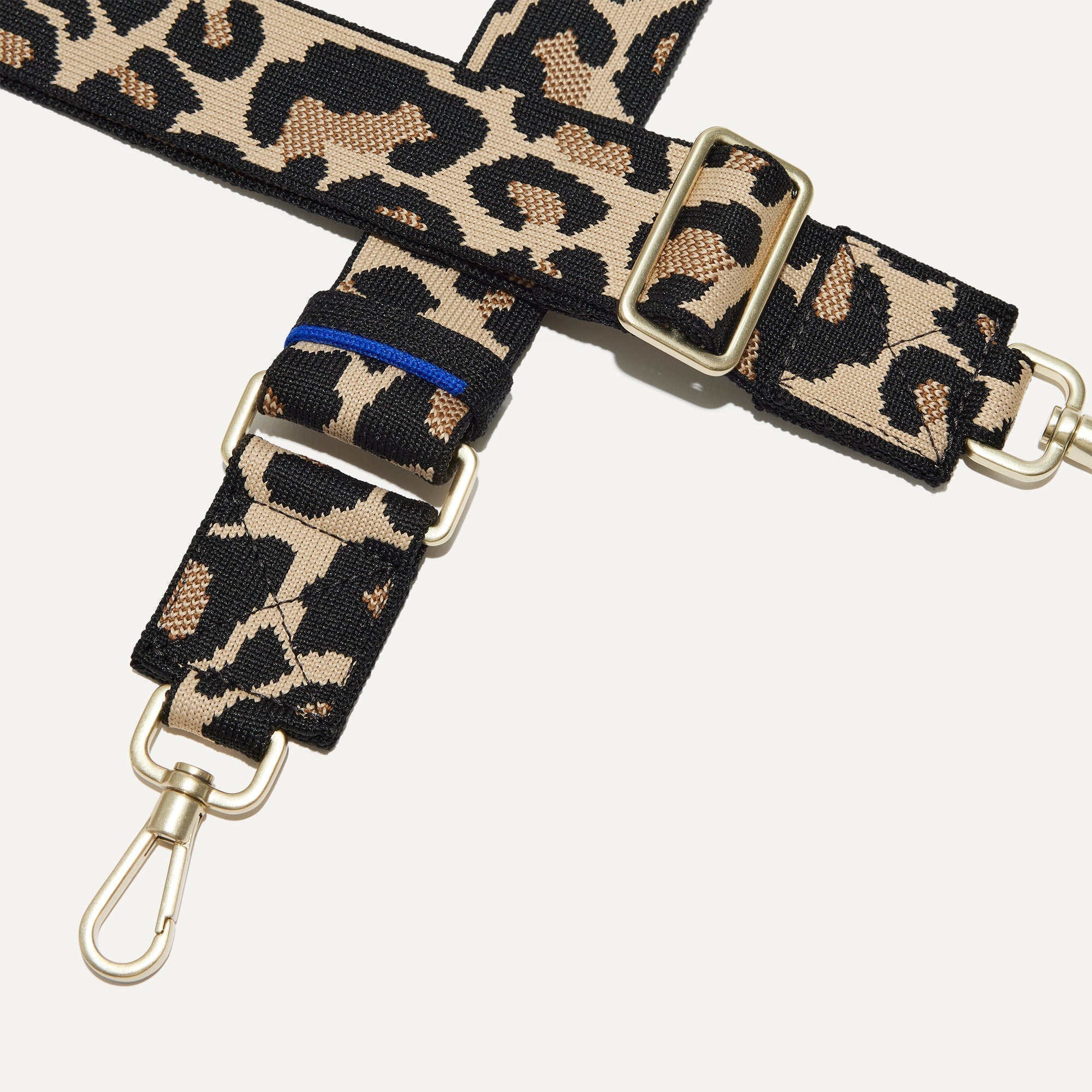 A closeup of The Crossbody Strap in Desert Cat, focusing on the end snap hooks and sliding buckle.
