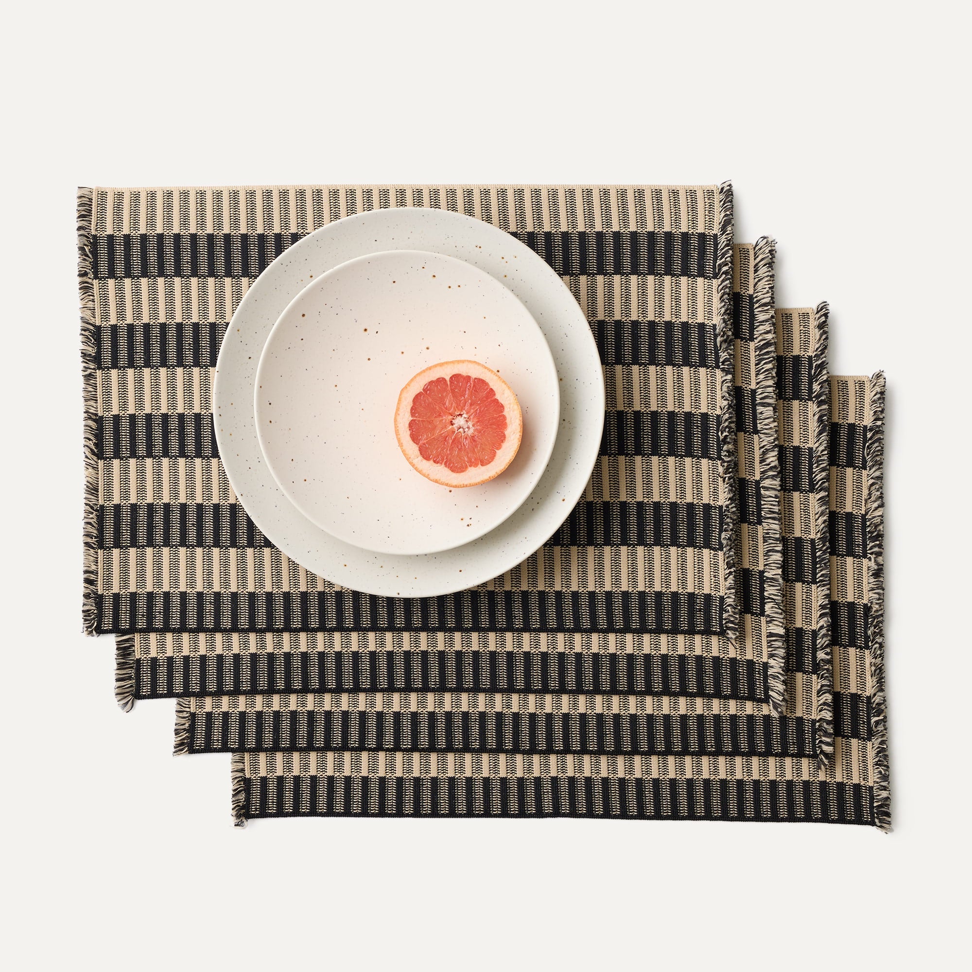 A set of four Placemats in Peppercorn Fringe shown with a plate setting.