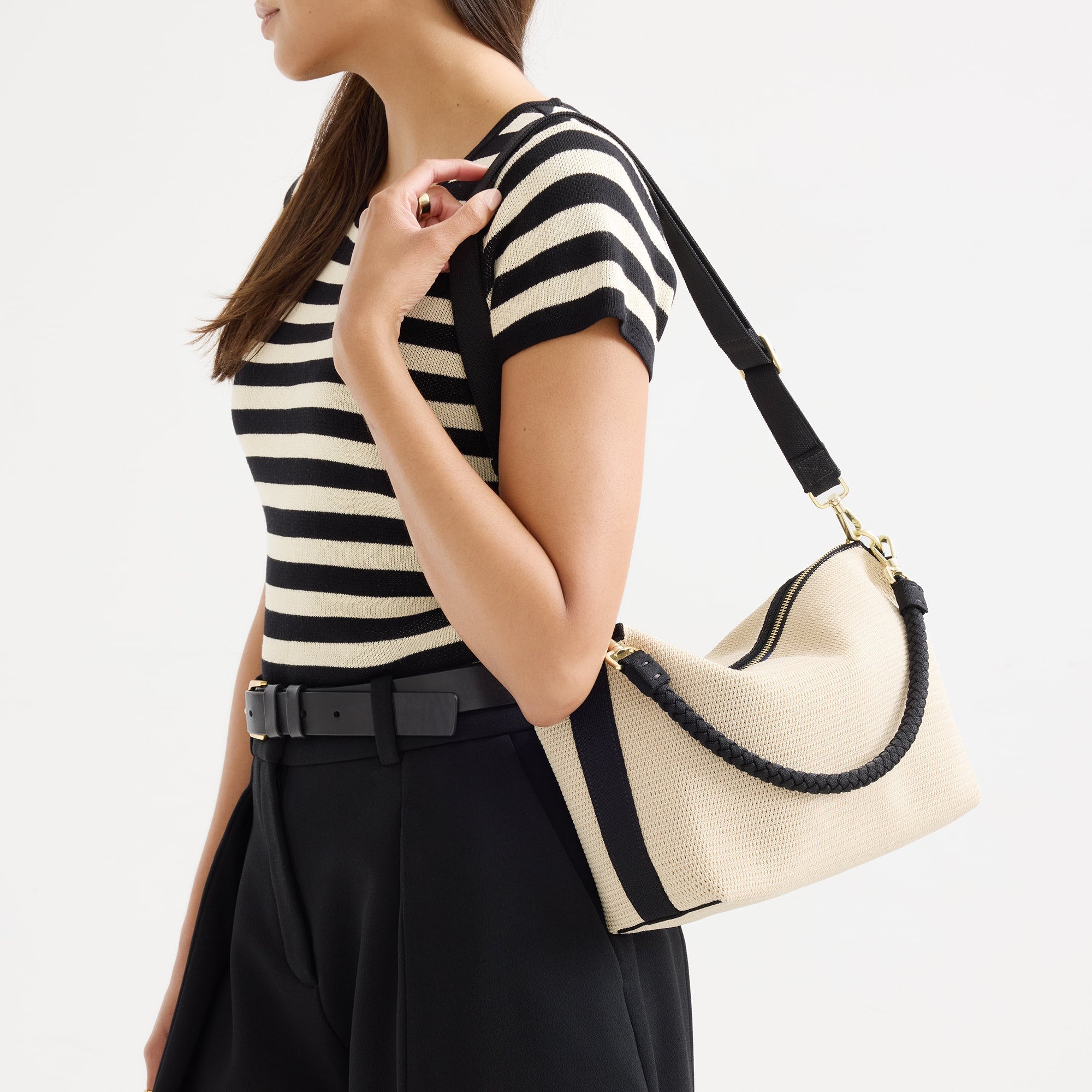 hover | The Daily Crossbody in Black and White Raffia-Knit, carried over the shoulder of a female model, shown from the right.