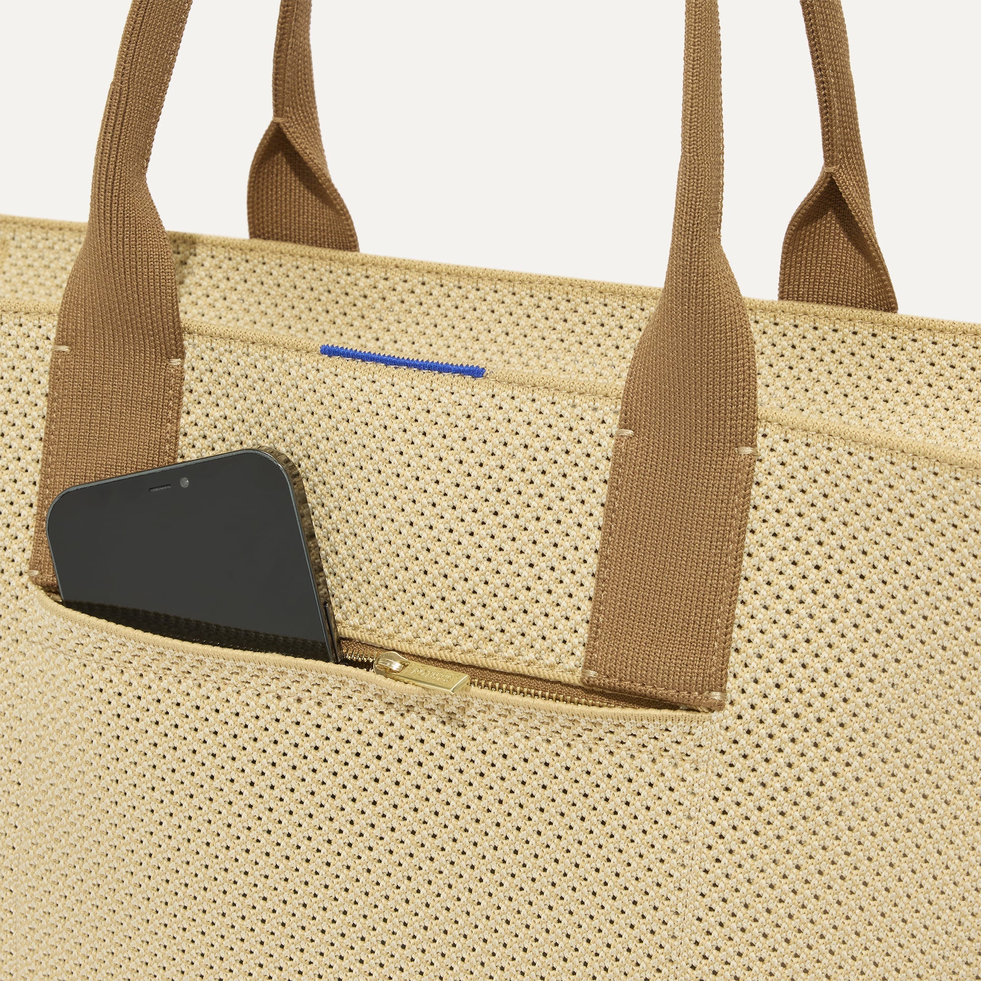 A closeup of The Classic Tote in Macadamia Open-Knit, focusing on the exterior zip pocket. 